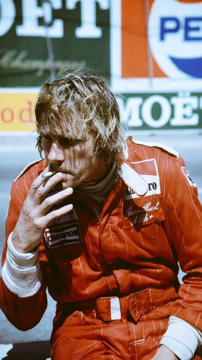 A racing driver in a red suit taking a break